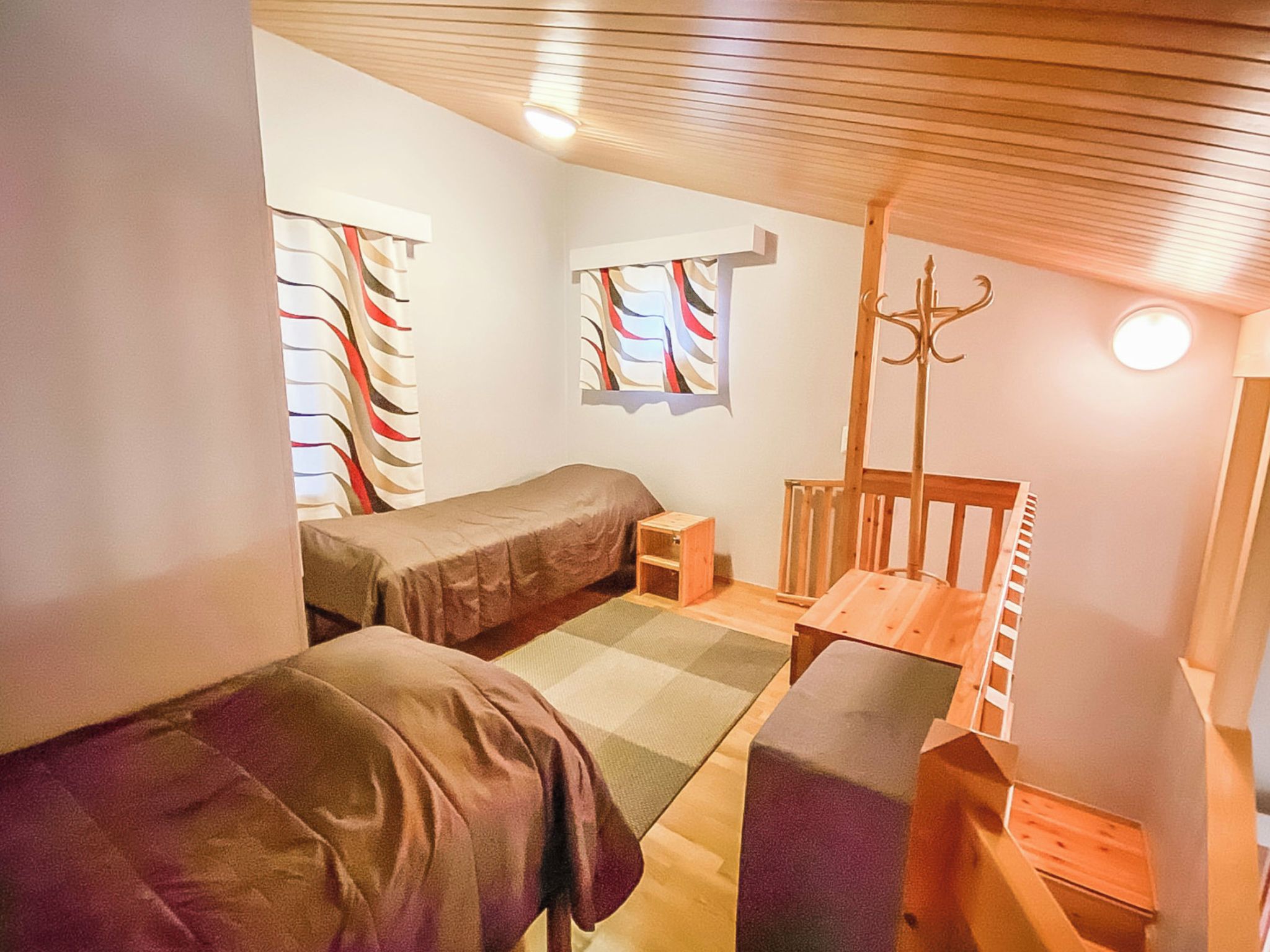 Une chambre à coucher de taille modeste, comprenant deux lits simples, une petite table en bois, une chaise et une fenêtre avec des rideaux.