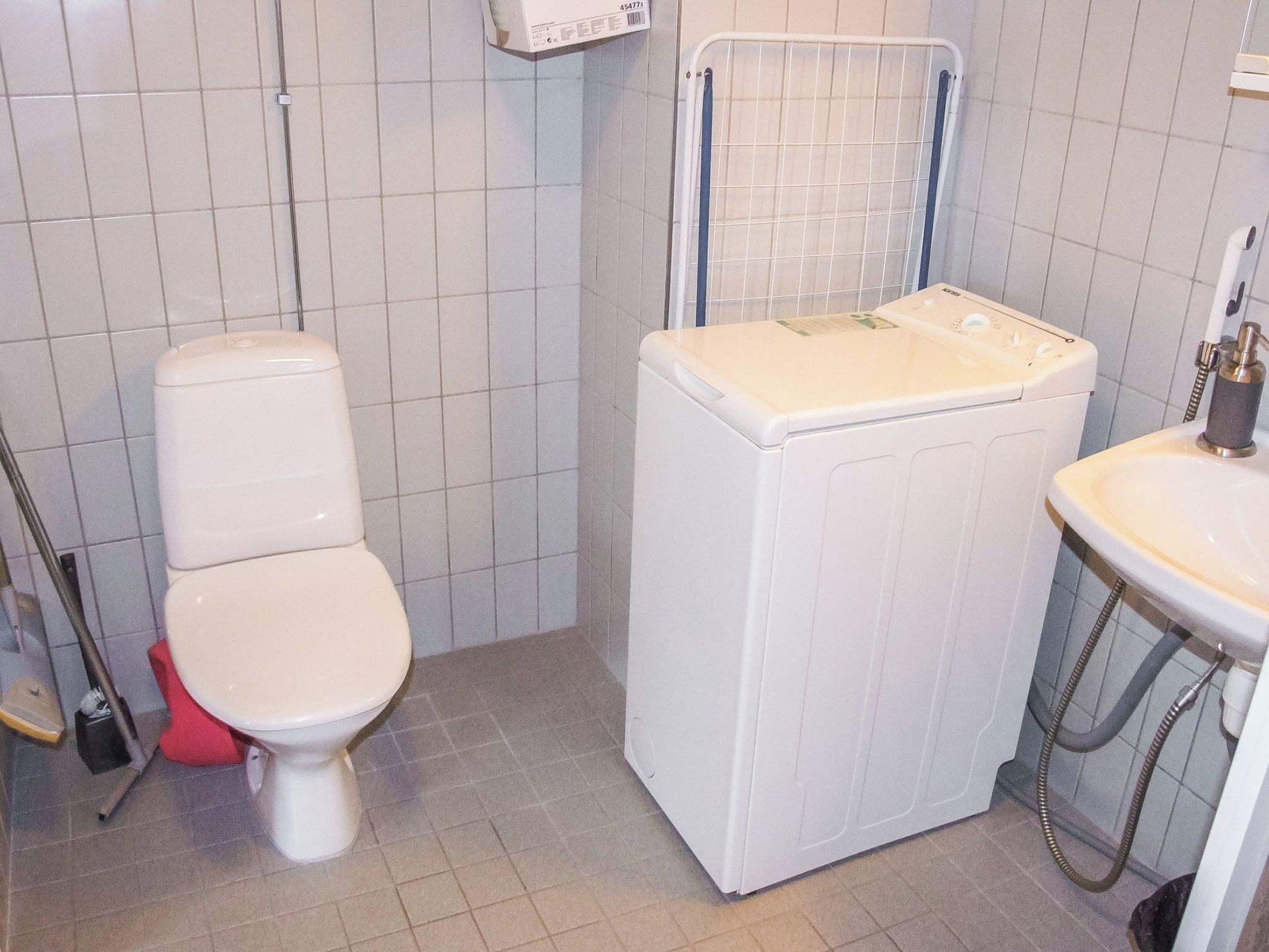 A small, compact bathroom with a toilet, washing machine, and sink.