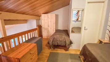 A bedroom with a wooden ceiling, a bunk bed, a single bed, a wooden bench, and a door with a window.
