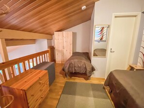 Un dormitorio con techo de madera, una litera, una cama individual, un banco de madera y una puerta con ventana.