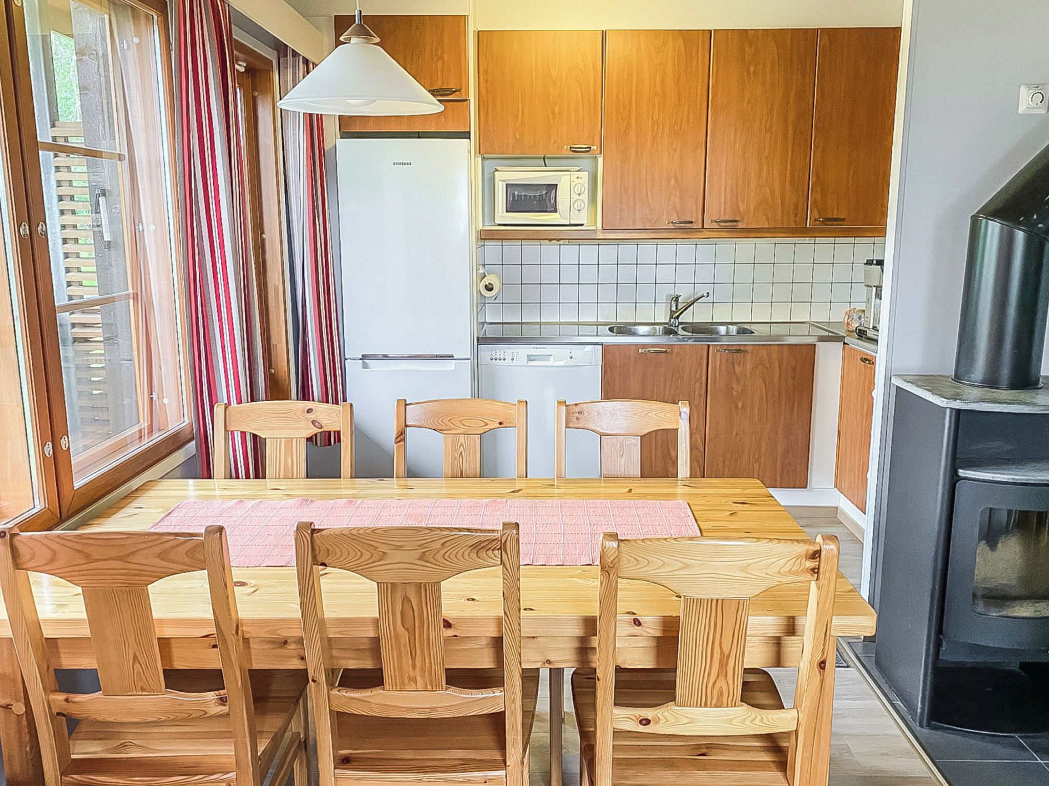 Kompakti keittiö, jossa on puiset kaapit, mikroaaltouuni, astianpesukone sekä ruokailutila, jossa on puinen pöytä ja tuolit.