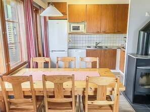 Cozinha compacta com armários de madeira, micro-ondas, lava-louças e área de refeições com mesa e cadeiras de madeira.
