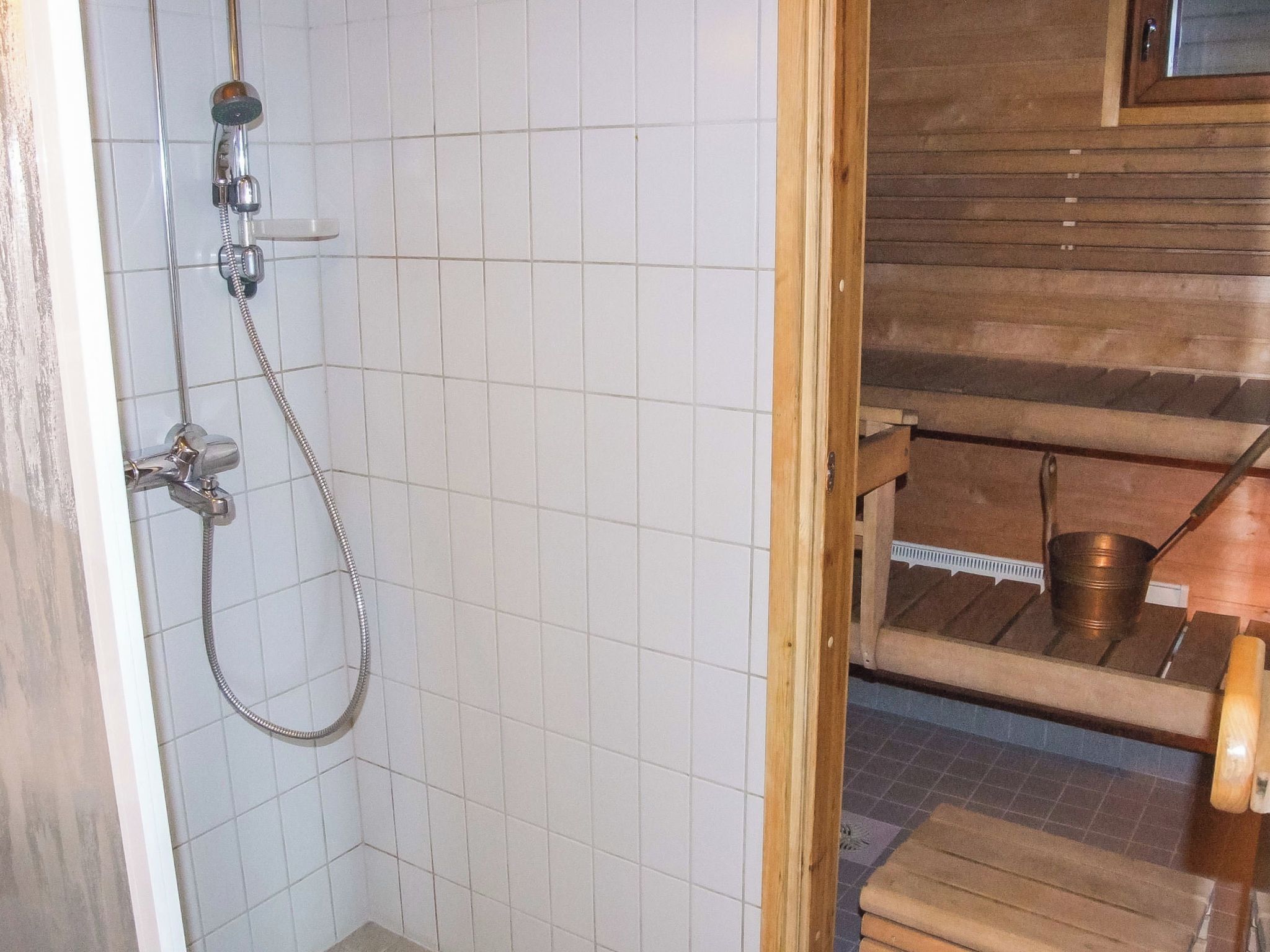Kylpyhuone, jossa on suihku, puinen hylly ja metallinen ämpäri.