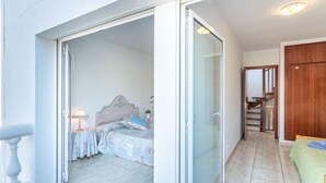 Un dormitorio con cama, mesita de noche y lámpara. Hay una puerta corrediza de vidrio que da a un balcón.