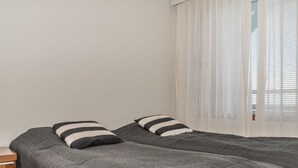 Ein Zimmer mit zwei Betten, jeweils mit einer dunkel gesteppten Bettdecke und gestreiften Kissen. Am Bett befindet sich ein Nachttisch.