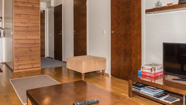 Ein modernes Wohnzimmer mit Holzboden, einer Couch, einem Couchtisch, einem Fernseher und einem Bücherregal.