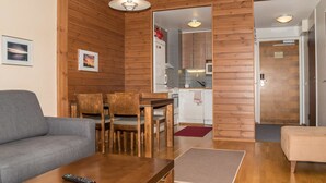 Ein modernes Wohnzimmer mit einer Couch, einem Esstisch und Stühlen. Durch einen offenen Durchgang ist eine Küche zu sehen, die eine Mikrowelle und Schränke beinhaltet.