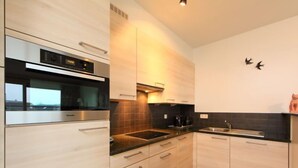 Una cocina moderna con armarios de madera clara, horno de acero inoxidable y encimera negra.