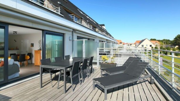 Una terraza moderna con comedor y sillones de descanso, con vista a una zona residencial.