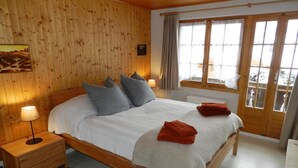 Une chambre aux murs lambrissés, avec un grand lit, deux tables de chevet et une fenêtre avec des rideaux.