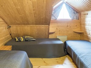 Una habitación de cabaña pequeña y de madera, con techo inclinado, una cama individual, dos mesitas de noche y un ventanal con vistas a árboles desnudos.