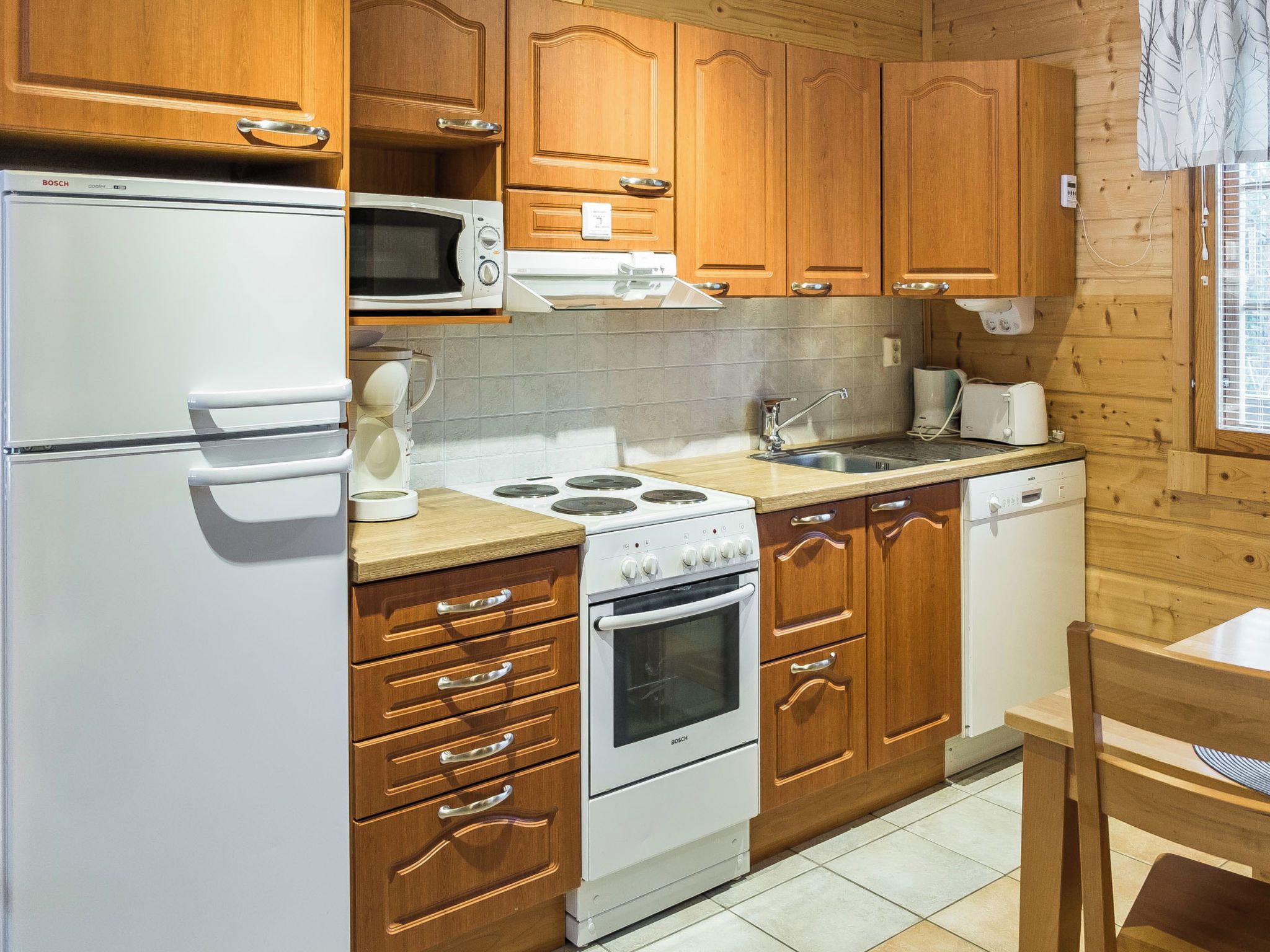 A compact kitchen with wooden cabinets, a Bosch refrigerator, a microwave, a stove, and a sink.
