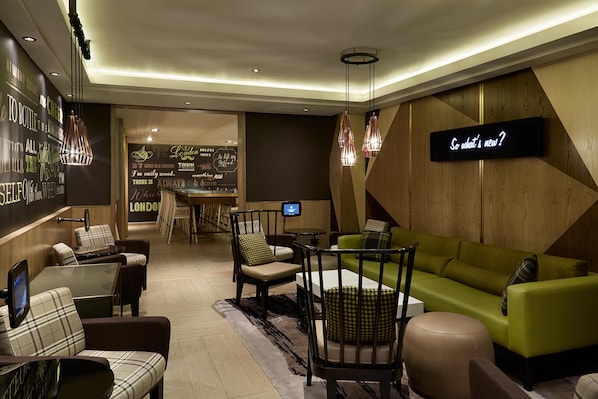 Un área de lounge moderna con asientos, un bar y un letrero digital que muestra '¿Qué hay de nuevo?'.