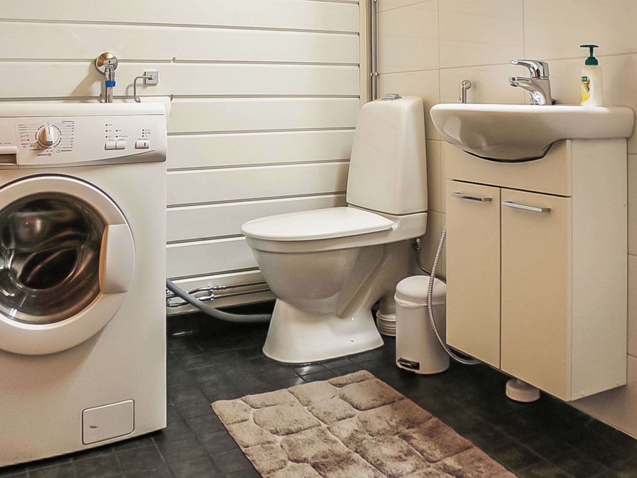 A compact bathroom with a washing machine, toilet, sink, and a telephone.