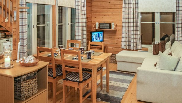A cozy cabin interior with a wooden dining table, chairs, a sofa, and a television. - Yllästokka 7 by Interhome (Ylläsjärvi)