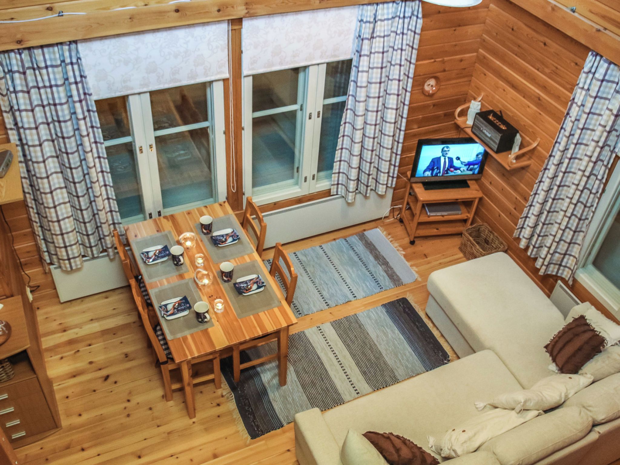 A cozy cabin interior with a wooden dining table set for four, a sofa, and a television on a wooden stand.
