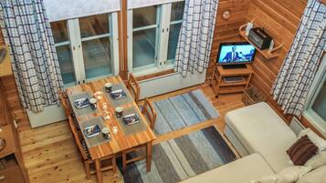A cozy cabin interior with a wooden dining table set for four, a sofa, and a television on a wooden stand.