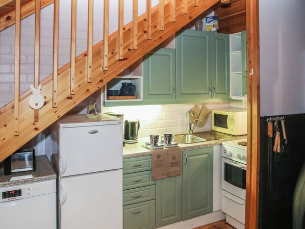 A compact kitchen with a wooden staircase, a Bosch refrigerator, a microwave, and green cabinets.