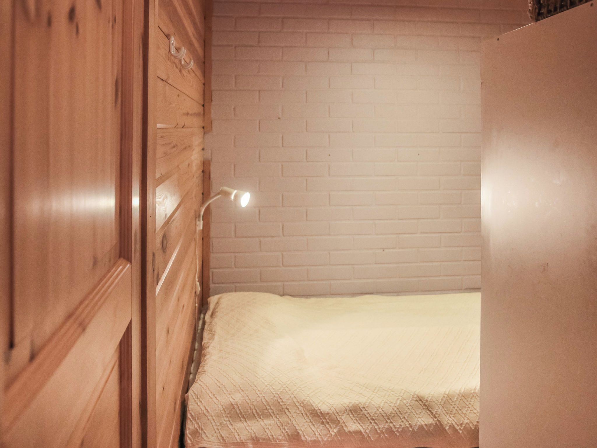 A room with a wooden wardrobe, a white brick wall, and a bed with a white blanket.