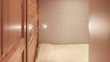 A room with a wooden wardrobe, a white brick wall, and a bed with a white blanket.