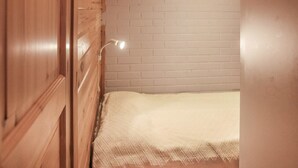 A small, single-bed room with a wooden wardrobe and a white brick wall. - Yllästokka 7 by Interhome (Ylläsjärvi)