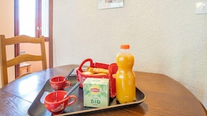 A dining table with a tray containing a carton of Lipton tea, a bottle of orange juice, and a basket of bread.