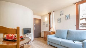 A compact living space with a dining area, a sofa, a television, and a small cabinet.