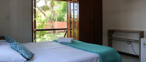 Un dormitorio con cama, almohadas, ventana y televisor.
