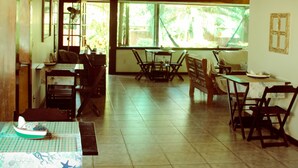 Un comedor espacioso con mesas y sillas de madera, ventanas amplias que dan a vistas de vegetación y un techo alto con vigas a la vista.