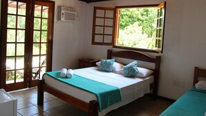 Un dormitorio con cama, almohadas, una mesita de noche, una ventana y una puerta.