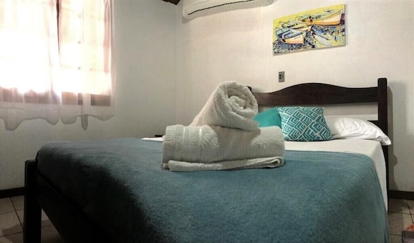 Una cama bien hecha con una colcha azul turquesa y una toalla blanca doblada encima.
