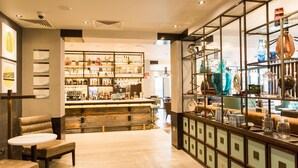 Una zona de bar con mostrador de madera, asientos y estanterías con botellas y vasos.