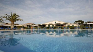 A swimming pool with lounge chairs and umbrellas, surrounded by buildings with a clear sky above. - Villaggio Turistico Residence La Cecinella (Cecina)