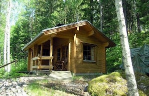 A wooden cabin with a porch, surrounded by trees.