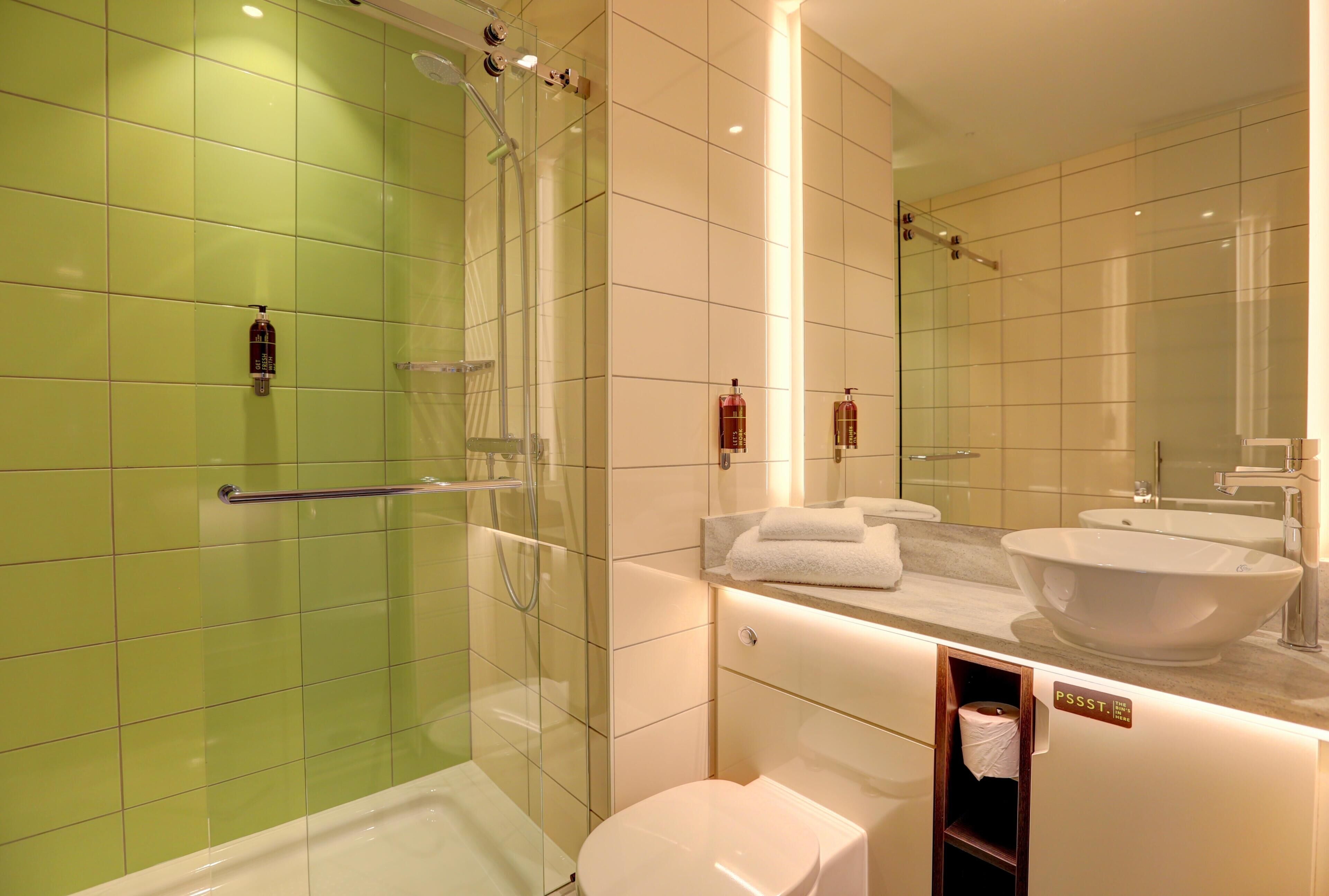 Une salle de bain moderne avec une douche à parois de verre, des toilettes blanches, un meuble-lavabo avec un grand évier et un miroir.