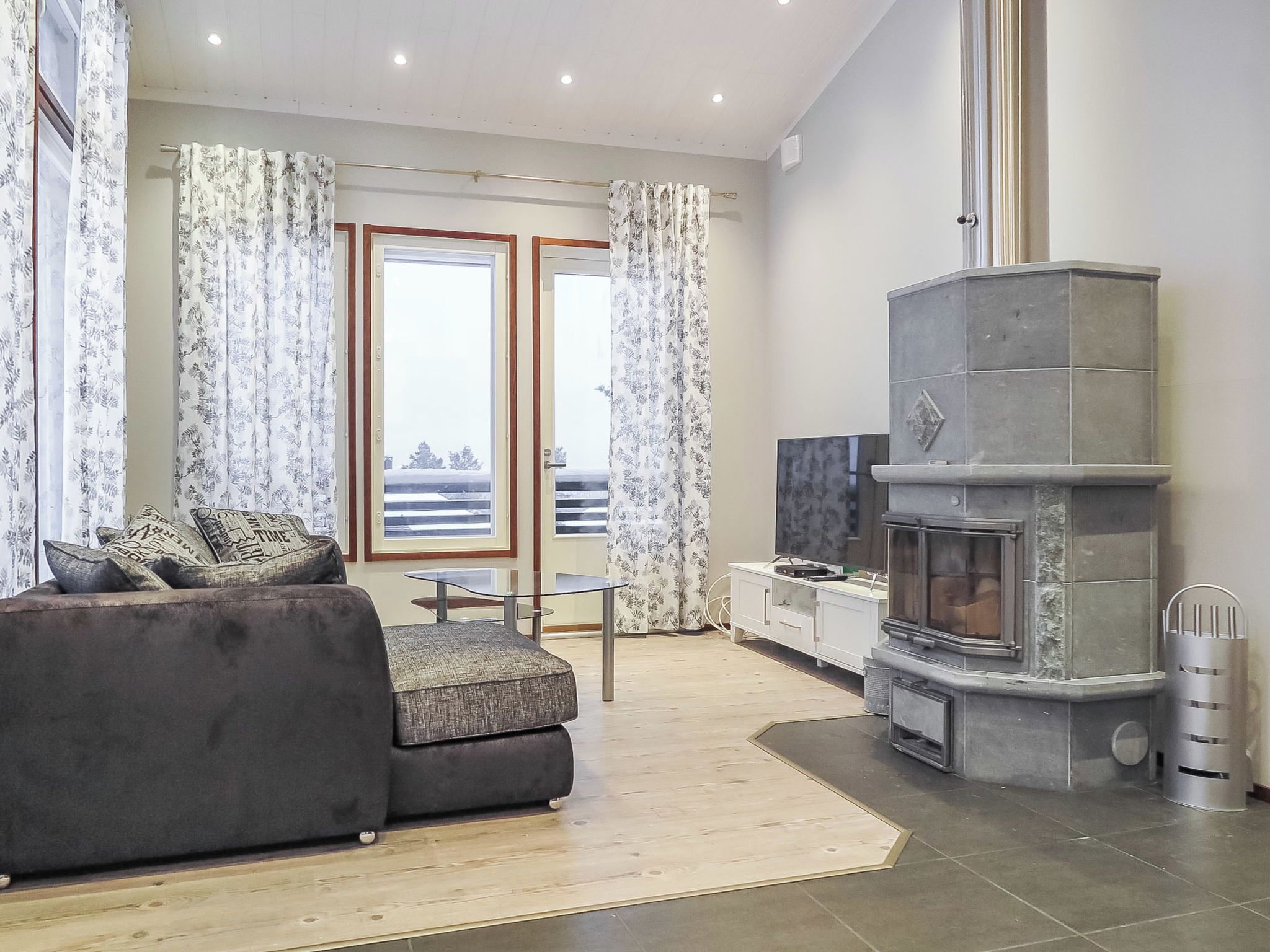 Un salon moderne avec un canapé, un téléviseur, une cheminée et un balcon agrémenté de rideaux.
