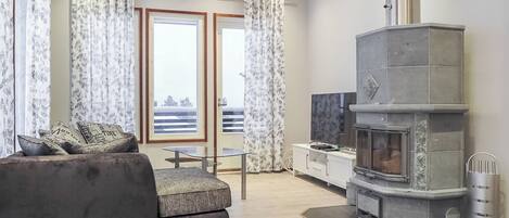 Un salon moderne avec un canapé, un téléviseur, une cheminée et un balcon agrémenté de rideaux.