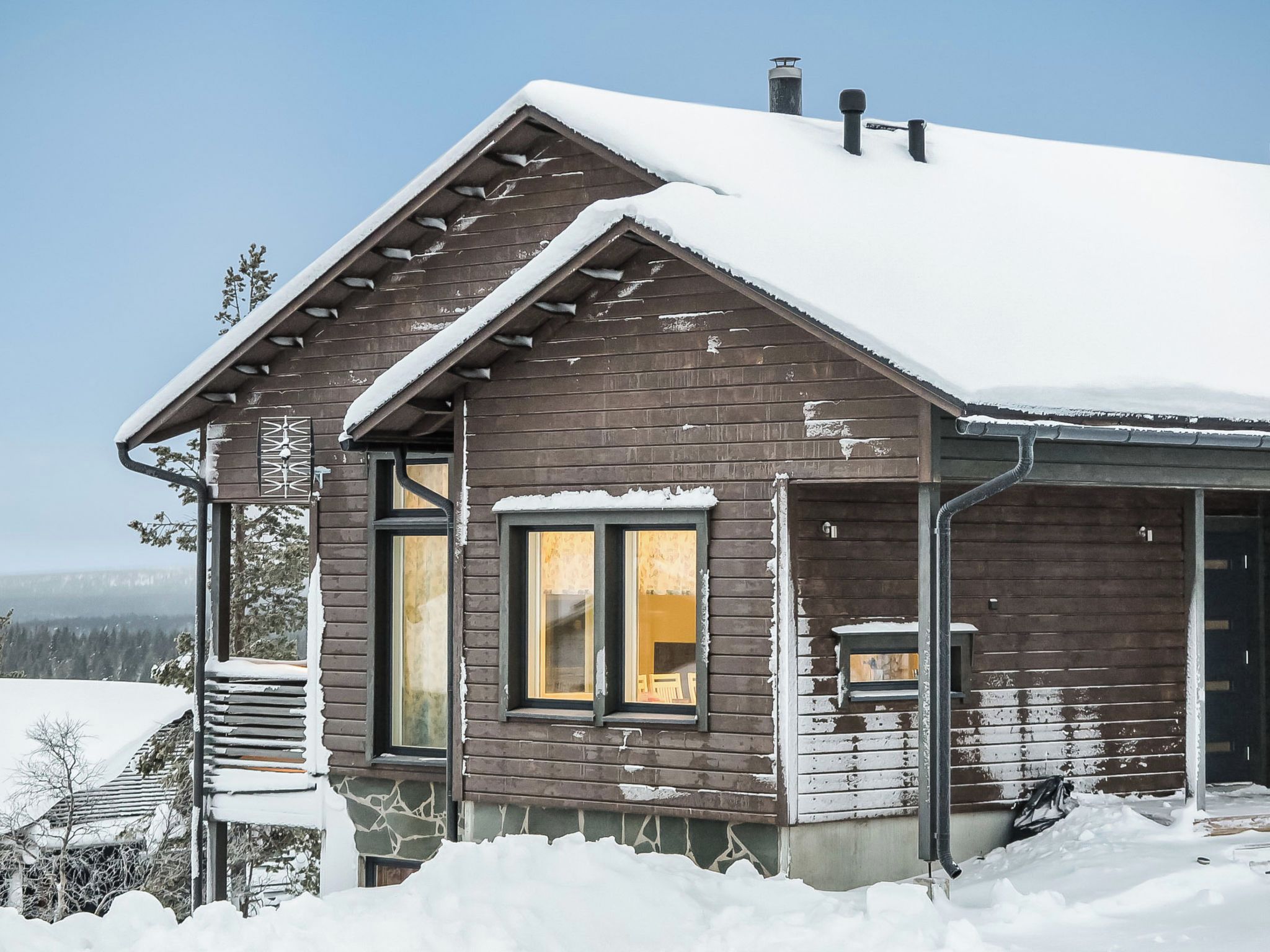 Een houten chalet met een schuin dak, grote ramen en een schoorsteen.