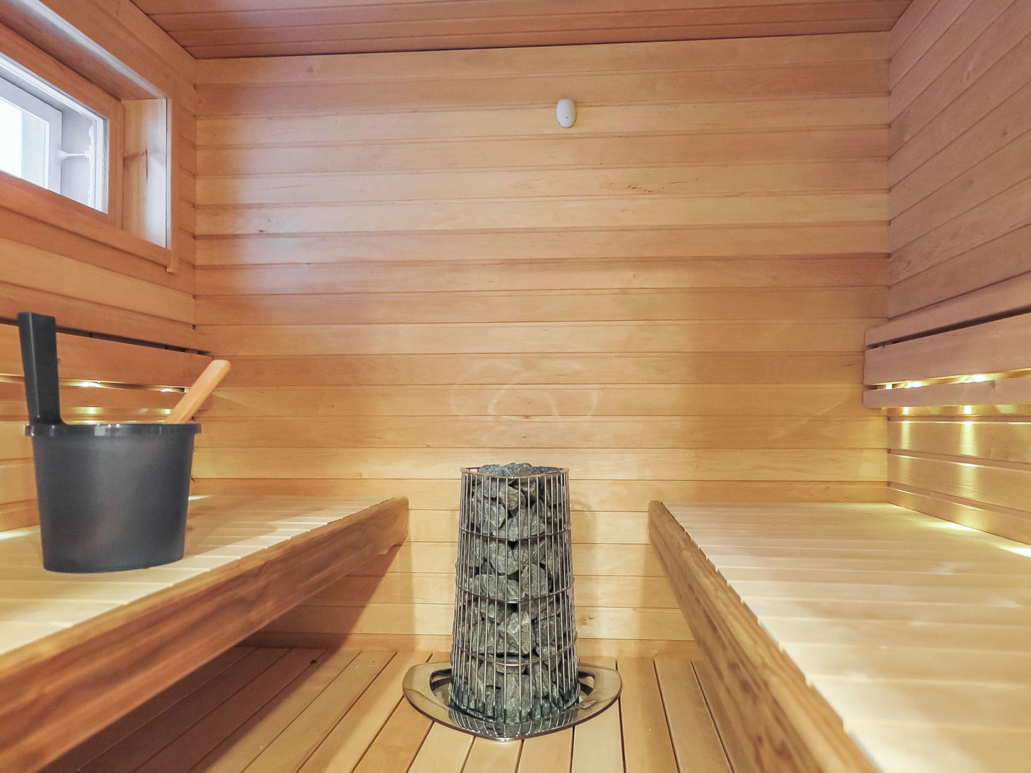 Sauna, jossa on puuseinät, penkki, kivillä täytetty astia ja ämpäri.