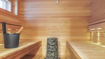 Sauna, jossa on puuseinät, penkki, kivillä täytetty astia ja ämpäri.