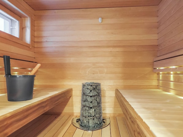 Een sauna met houten wanden, een bank, een stenen bak en een emmer.