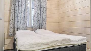 Huone, jossa on sänky, ikkuna, jossa on verhot, ja puuseinät.