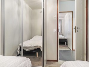 A narrow hallway with a bed at the end, a door with a mirror, and a light switch on the wall.