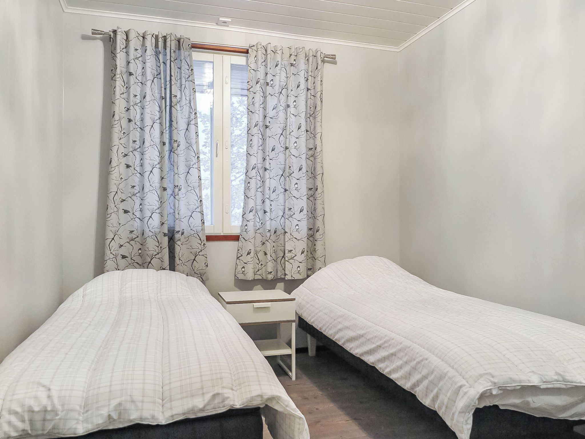 Une chambre avec deux lits simples, une petite table et une fenêtre avec des rideaux.