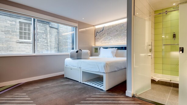 A modern hotel room with a bed, a map on the wall, a window, and a shower area. - Hub By Premier Inn London City Bank (London)
