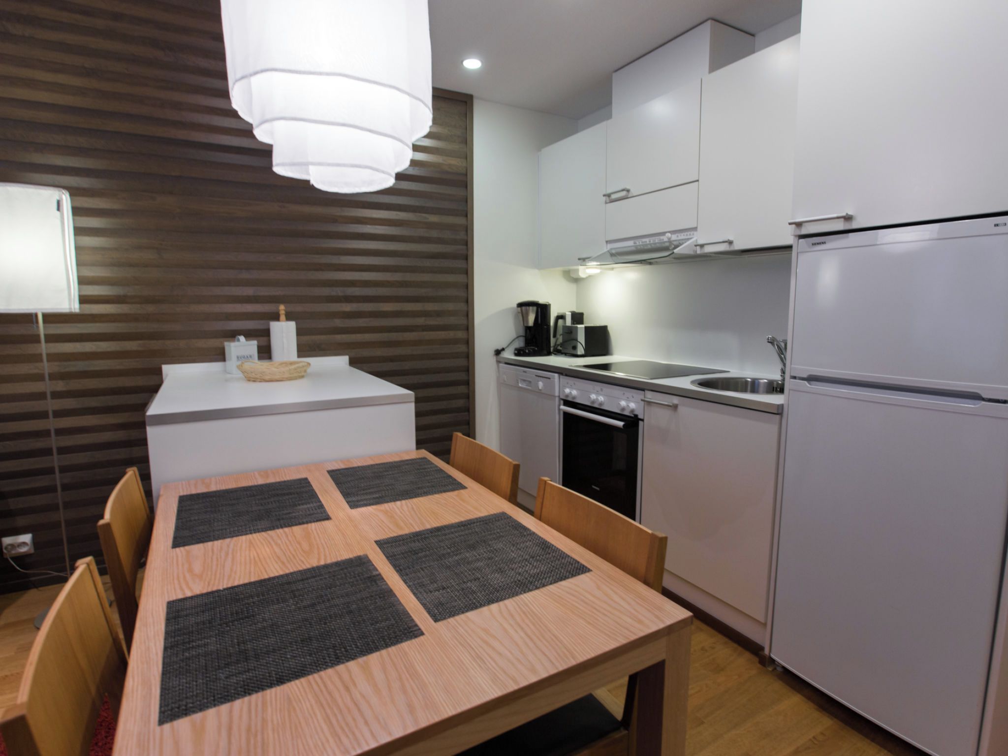 Una cocina compacta con una mesa de comedor, sillas, un refrigerador y una cafetera.