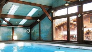 An indoor swimming pool with wooden beams and large windows. - Les Hauts des Chavants - by Interhome (Les Houches)
