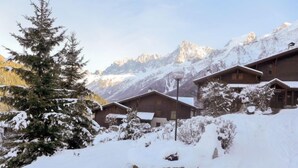 A snow-covered mountain lodge with wooden cabins, surrounded by snow-laden trees and mountains in the background. - Les Hauts des Chavants - by Interhome (Les Houches)