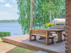 Een houten terras met een bank en picknicktafel, met uitzicht op een meer en bomen op de achtergrond.