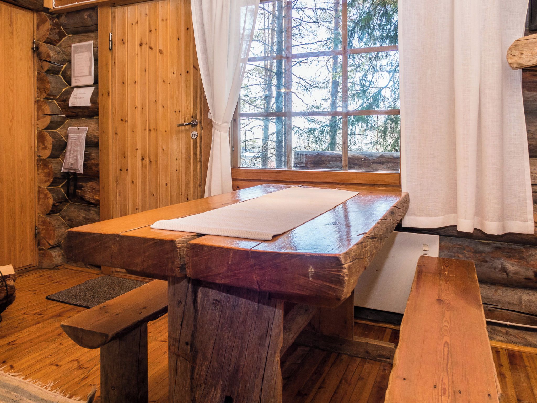 L’intérieur d’un chalet rustique en bois, avec un mur en pierre, une table en bois, un banc et une fenêtre donnant sur les arbres.